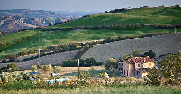 Veduta del Podere La Castellina immerso nelle colline della Val d'Orcia, con la piscina sulla sinistra